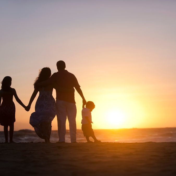 family on beach with sunset holding hands
