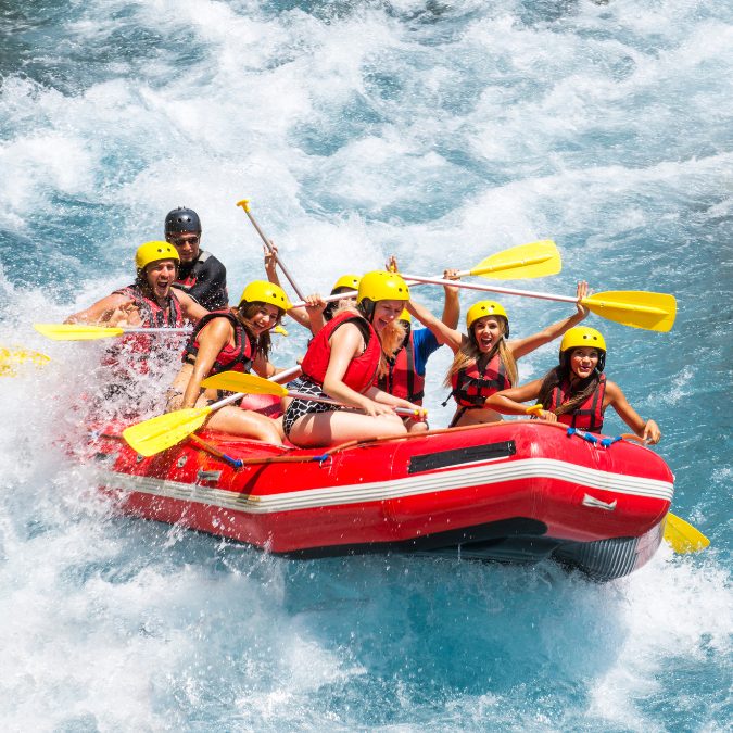 people smiling on a white water raft with yellow paddles and red boat