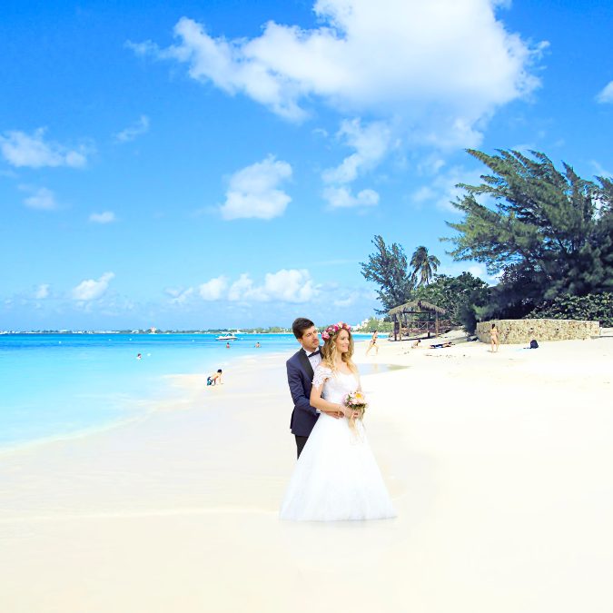 married couple standing on beach with trees and ocean in background 