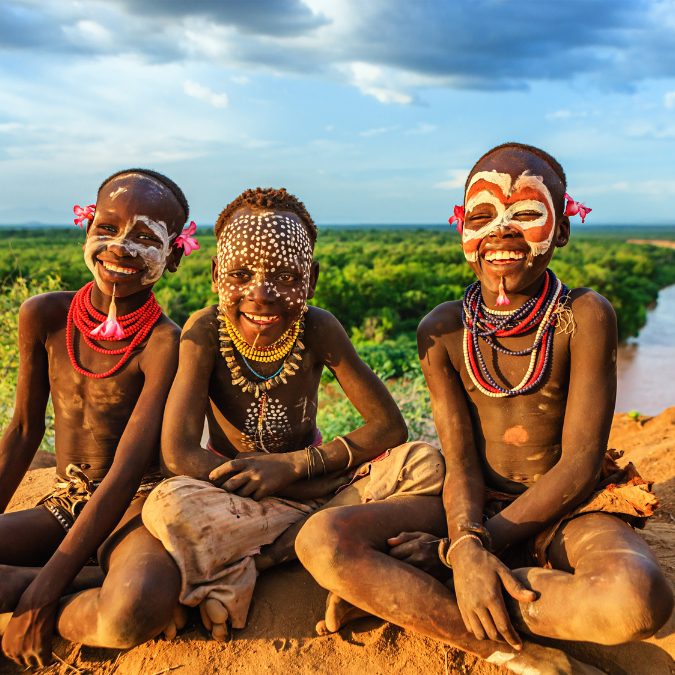 3 children with face paint sitting in the sun smiling 