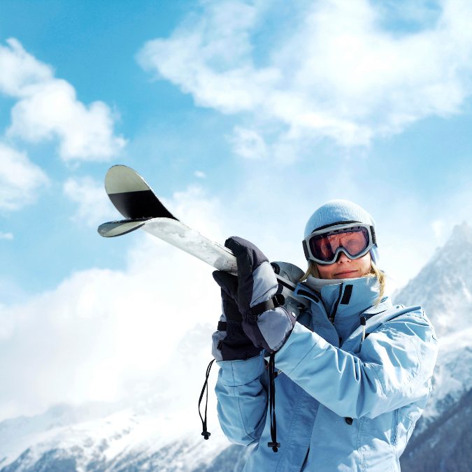 lady holding skies in ski gear in the mountains