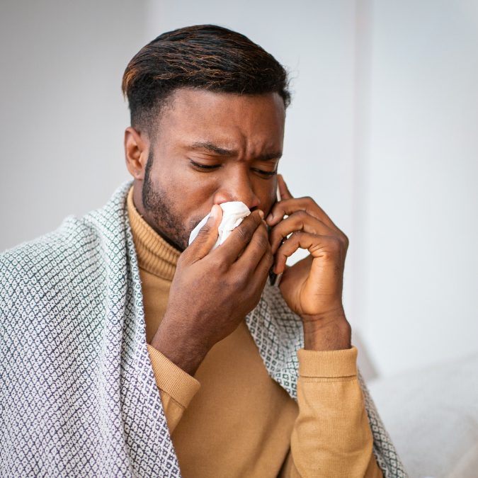 man with a blanket over him while blowing his nose 
