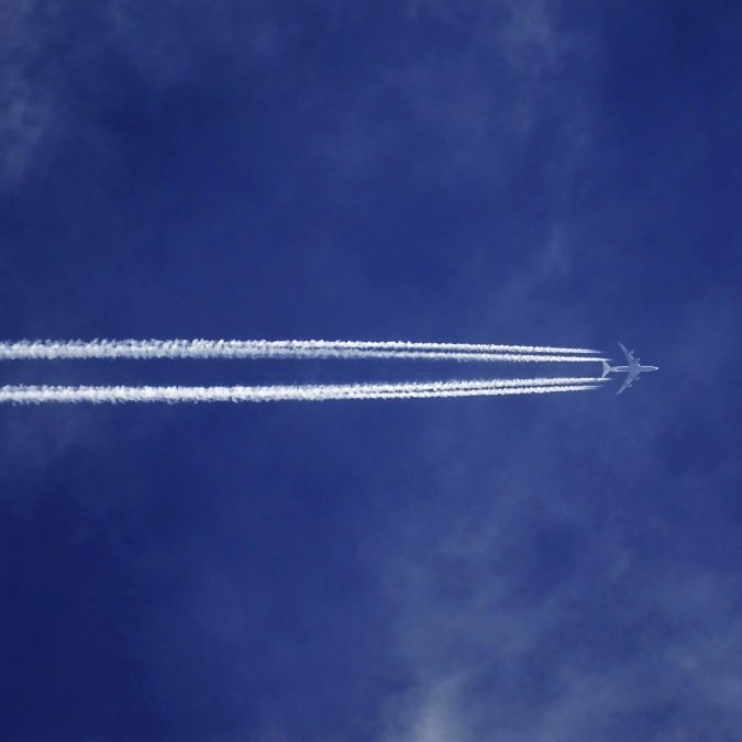 plane in the sky from below with blue sky around leaving jet trail