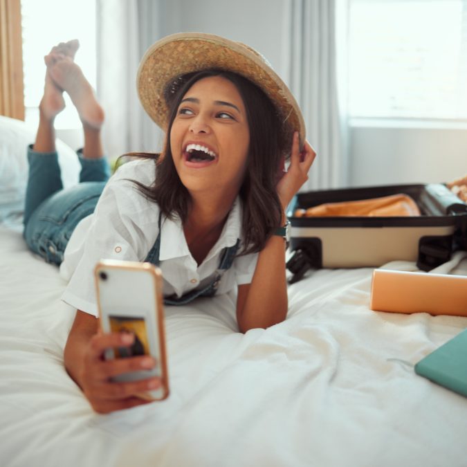 woman on bed holding phone while smiling 