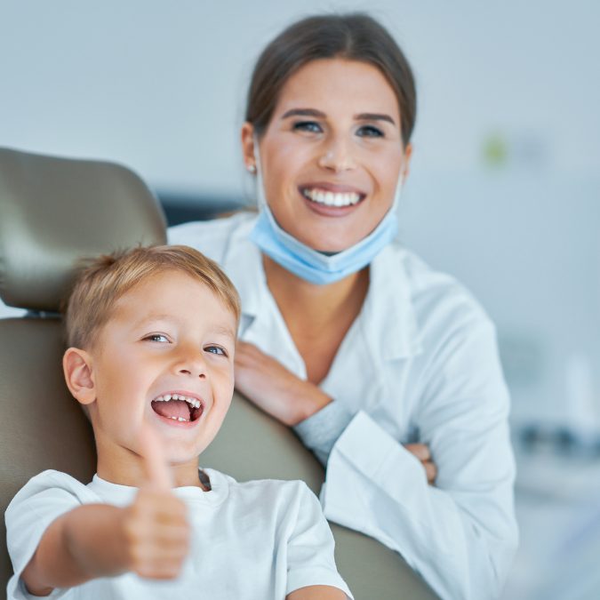child smiling with thumbs up with dentist behind him