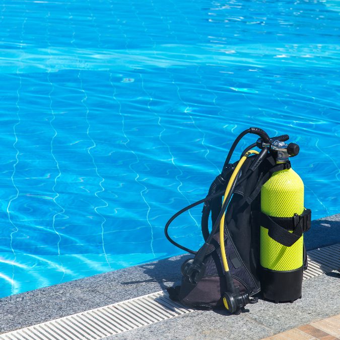 one green scuba diving tank and bcd in front of pool 