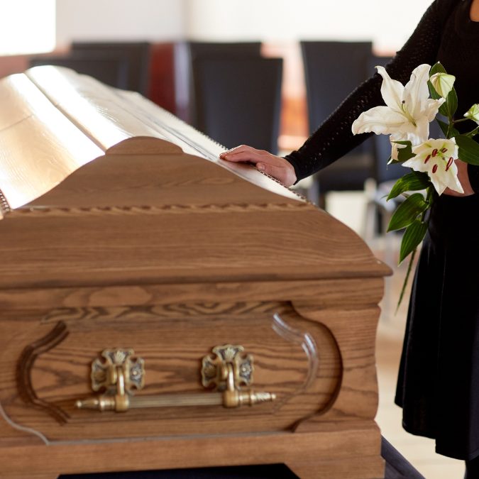 coffin at a funeral with a man's hand on it 