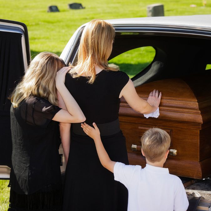 family mourning at a funeral with woman's hand on the coffin 