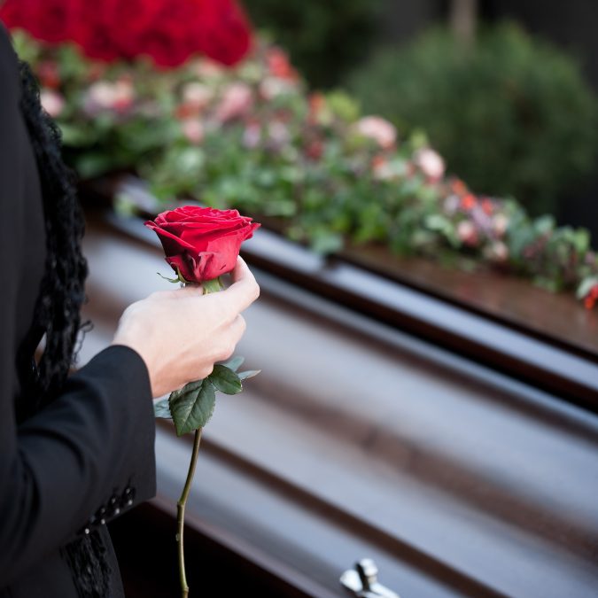 a woman's holding a rose in front of a coffin 