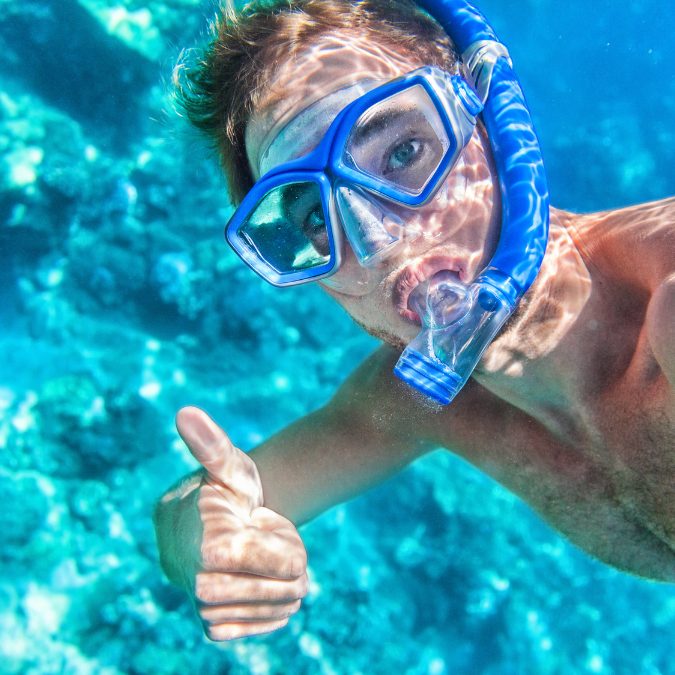 man snorkeling with a blue mask giving thumbs up tp the camera Snorkel