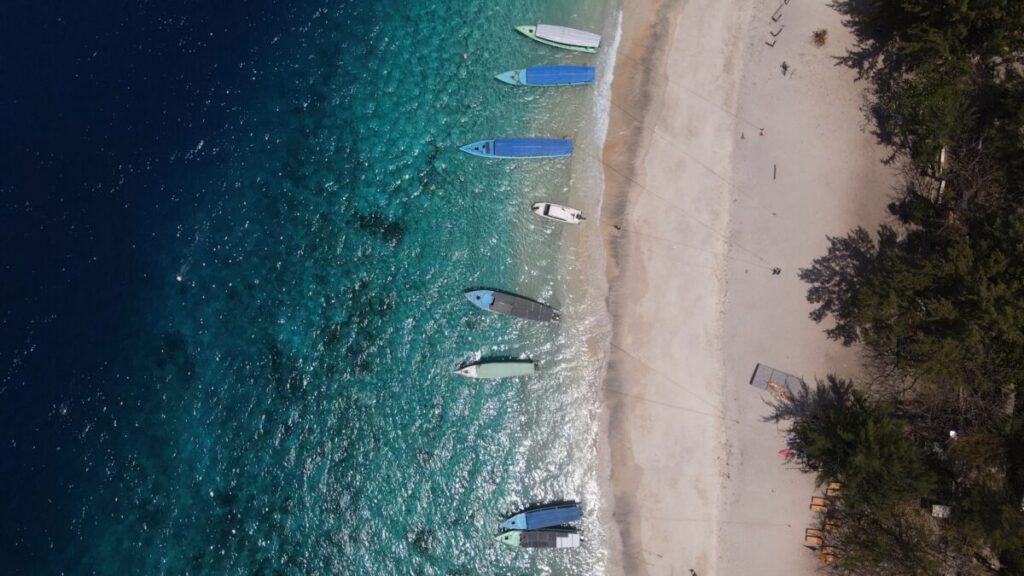 top down shot of blue water and white beach with boats in the water
